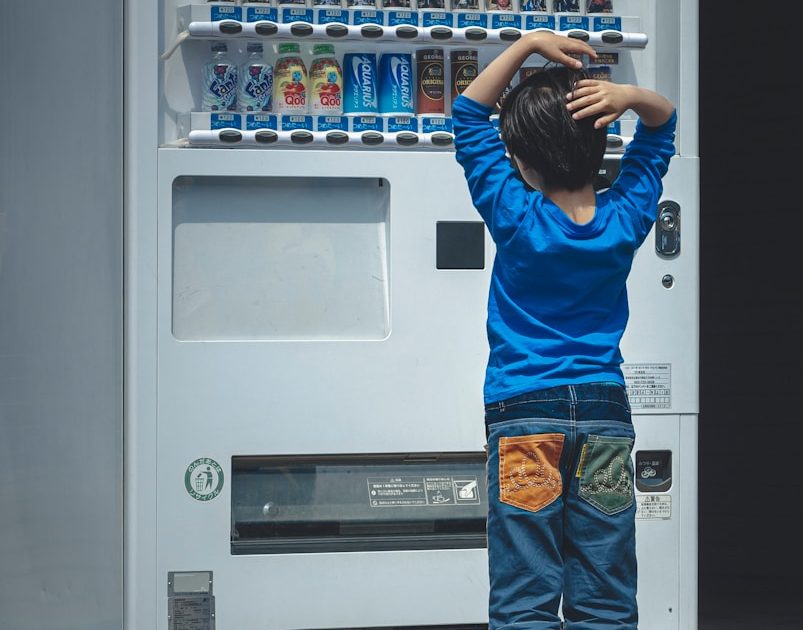 Photo by Egor Myznik a young boy standing in front of a vending machine